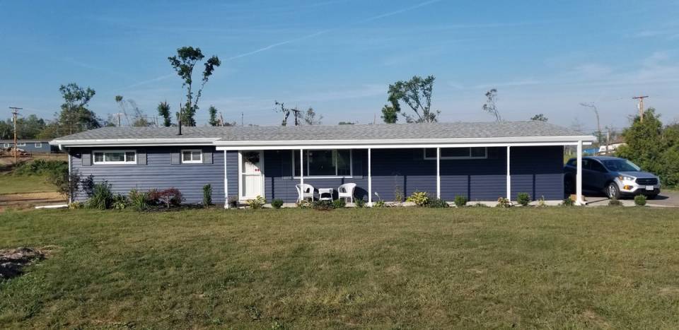 The finished ranch house from the front lawn in blue vinyl siding with a white porch, Beavercreek, Ohio.